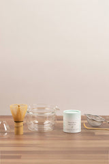 Tea-making tools including a whisk, bowl, and container on a wooden surface with a plain background