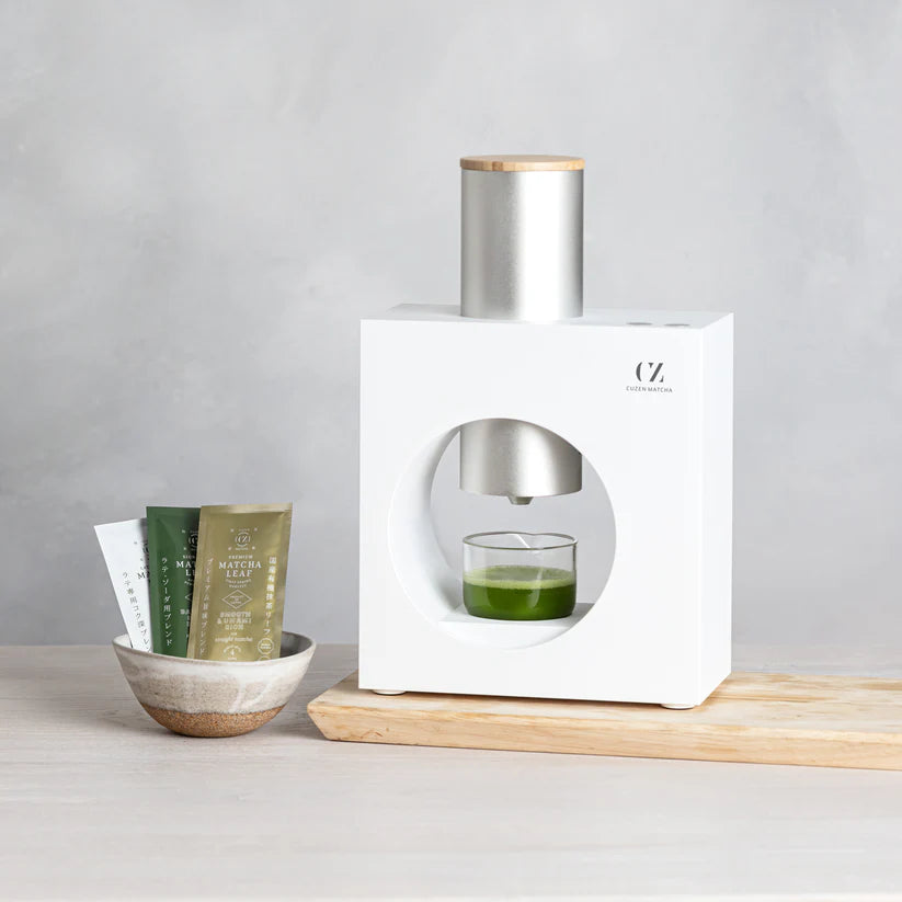 White bottle with silver cap on a wooden surface, with a glass of green liquid and small containers nearby.