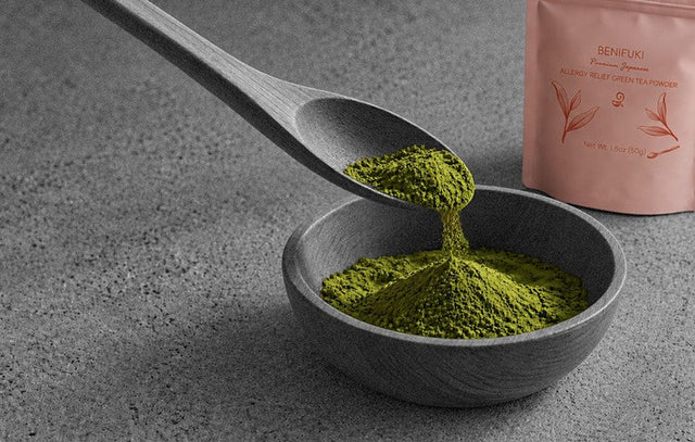 Benifuki allergy relief green tea powder in the new 50g pouch beside a stone bowl of the powder and a wooden spoon