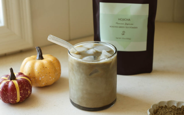 Iced pumpkin spice hojicha latte with small pumpkins and a bag of hojicha powder