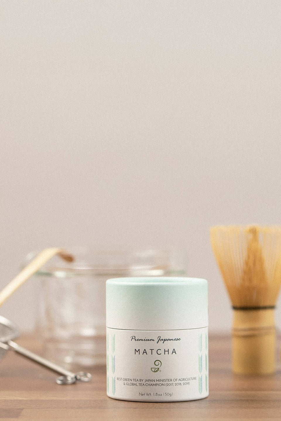 Matcha powder container on a wooden surface with tea-making tools in the background